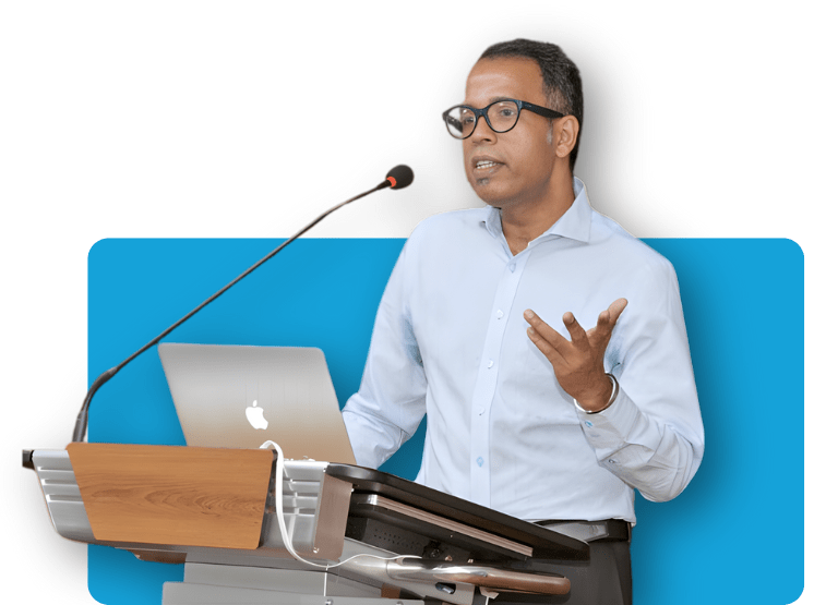 Portrait of Dr. Parthopratim Dutta Majumder, Secretary of the Uveitis Society of India (USI), speaking at a podium with a microphone and laptop. He is also the Head of Innovation at Sankara Nethralaya, Founder of eOphtha, and a member of the International Uveitis Study Group, specializing in ocular inflammatory diseases.